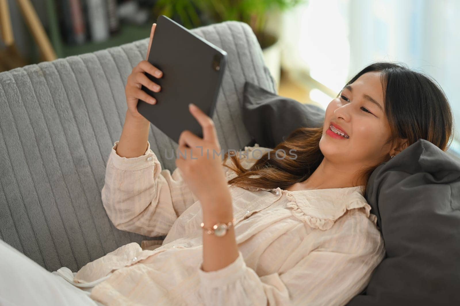 Relaxed young woman in casual clothes lying on couch and using digital tablet
