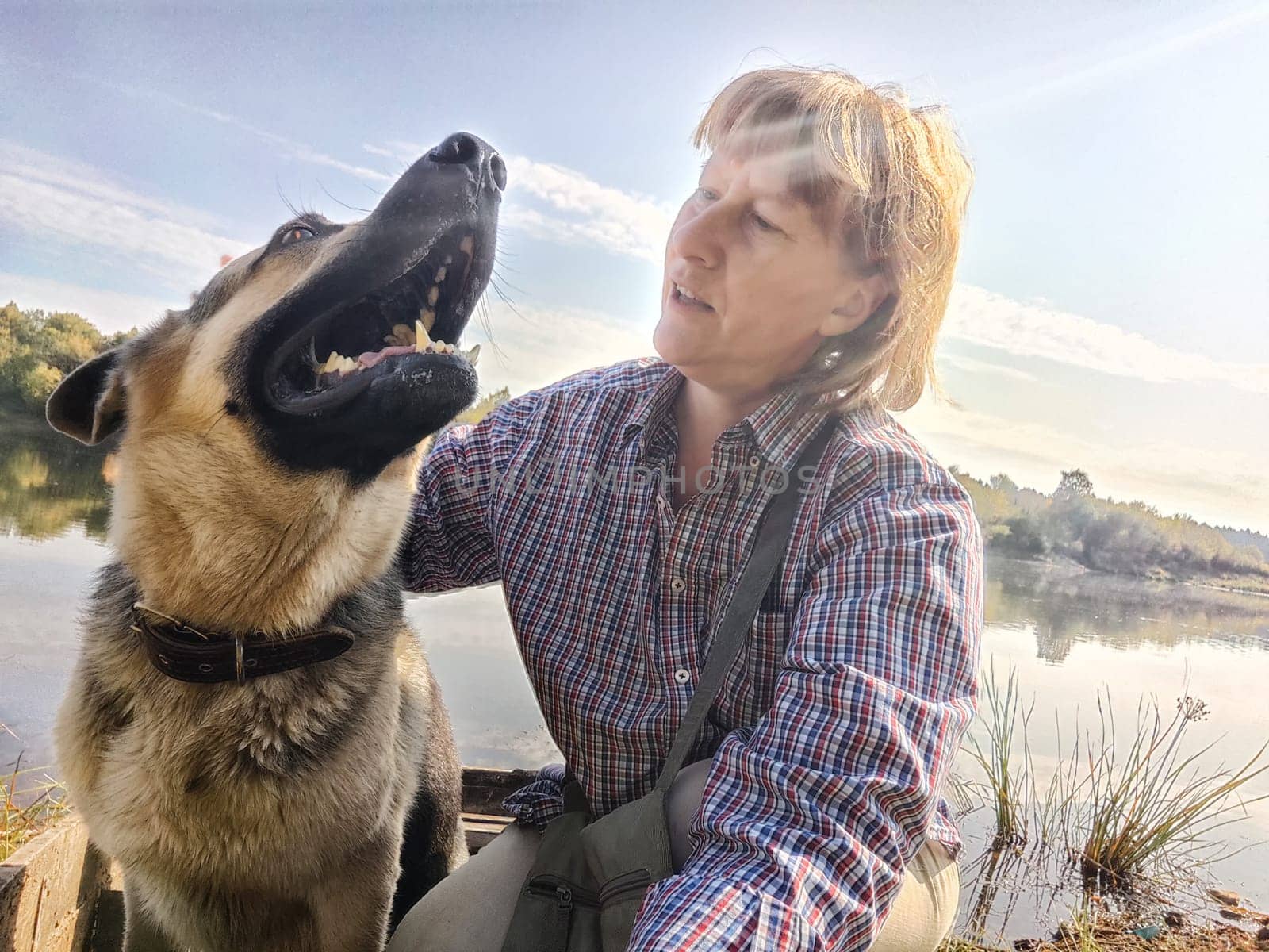 Adult girl with shepherd dog taking selfie in forest. Middle aged woman and big shepherd dog on nature. Friendship, love, fun, hugs