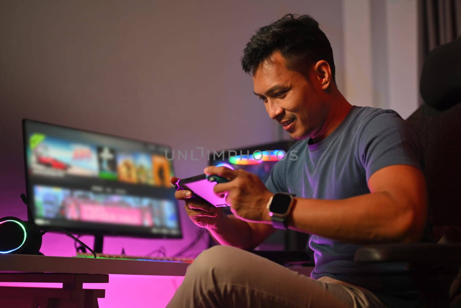 Smiling young man playing video games in his bedroom with neon led lights. Gaming, esports and tournament concept.