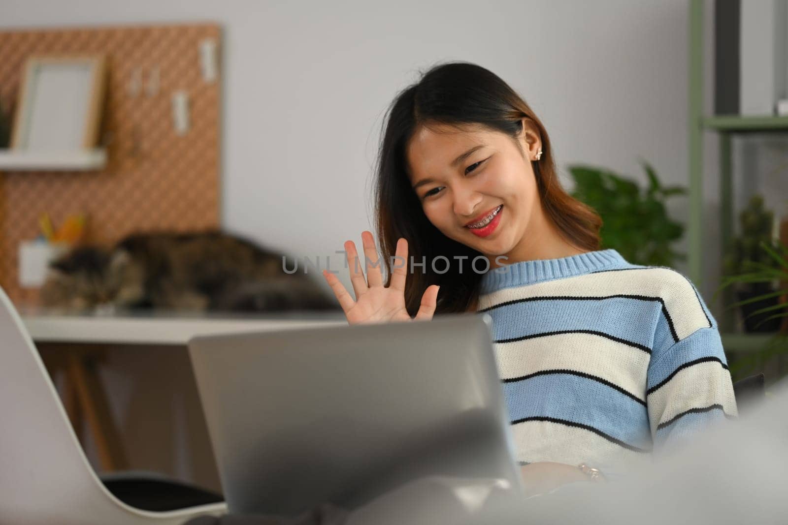 Smiling young woman enjoying pleasant conversation, making video call on laptop. by prathanchorruangsak