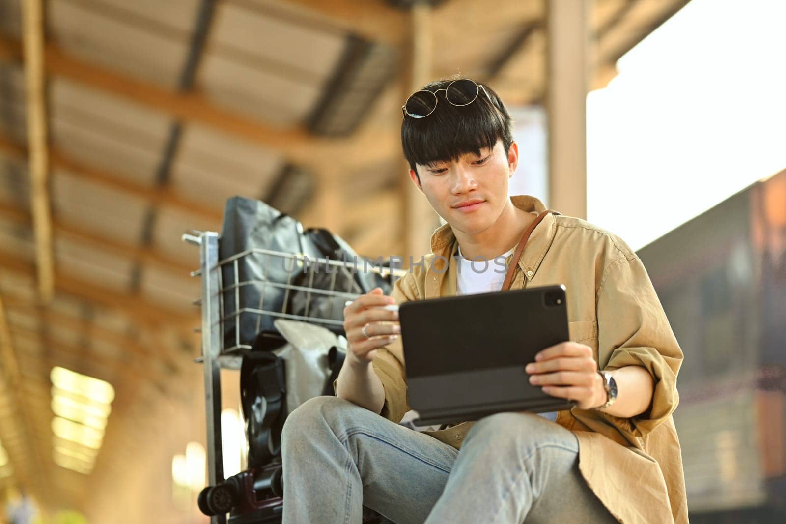 Young man using digital tablet, checking the route of trip on map while waiting train
