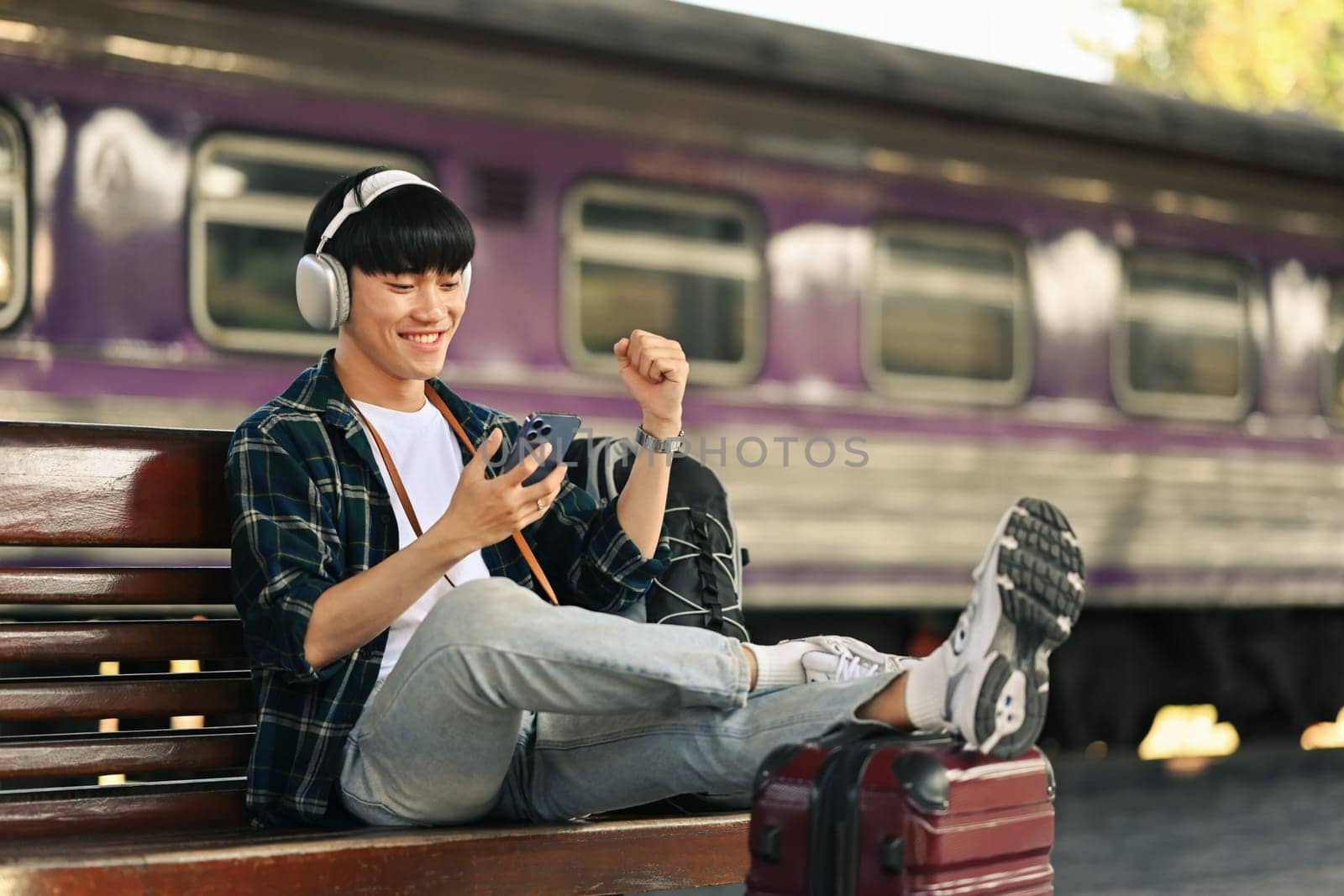 Young man sitting on bench and using mobile phone, waiting for the train on the platform. by prathanchorruangsak