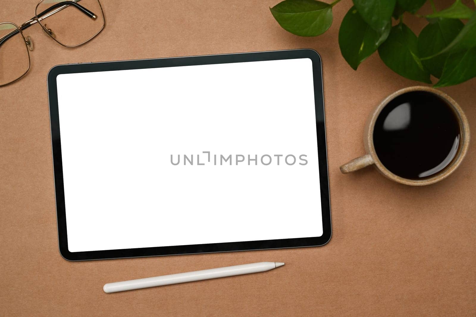 Top view digital tablet with white empty screen, coffee cup and glasses on brown background.