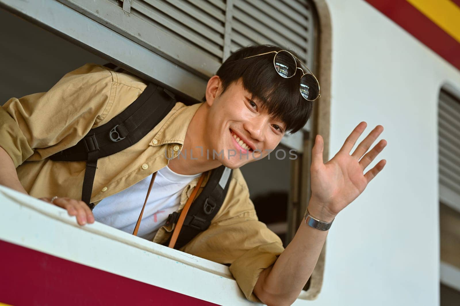 Happy Asian male backpacker waving from the train window. Transportation, people and traveling concept. by prathanchorruangsak