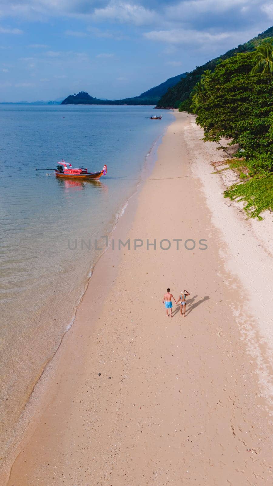 A beautiful view of a calm beach with crystal clear water on the blue sky at Koh Libong, Trang province, Thailand, Andaman Sea. A couple of men and woman walking on the beach