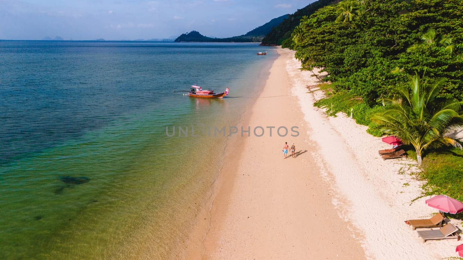 A beautiful view of a calm beach with crystal clear water on the blue sky at Koh Libong, Trang province, Thailand, Andaman Sea. A couple of men and woman walking on the beach