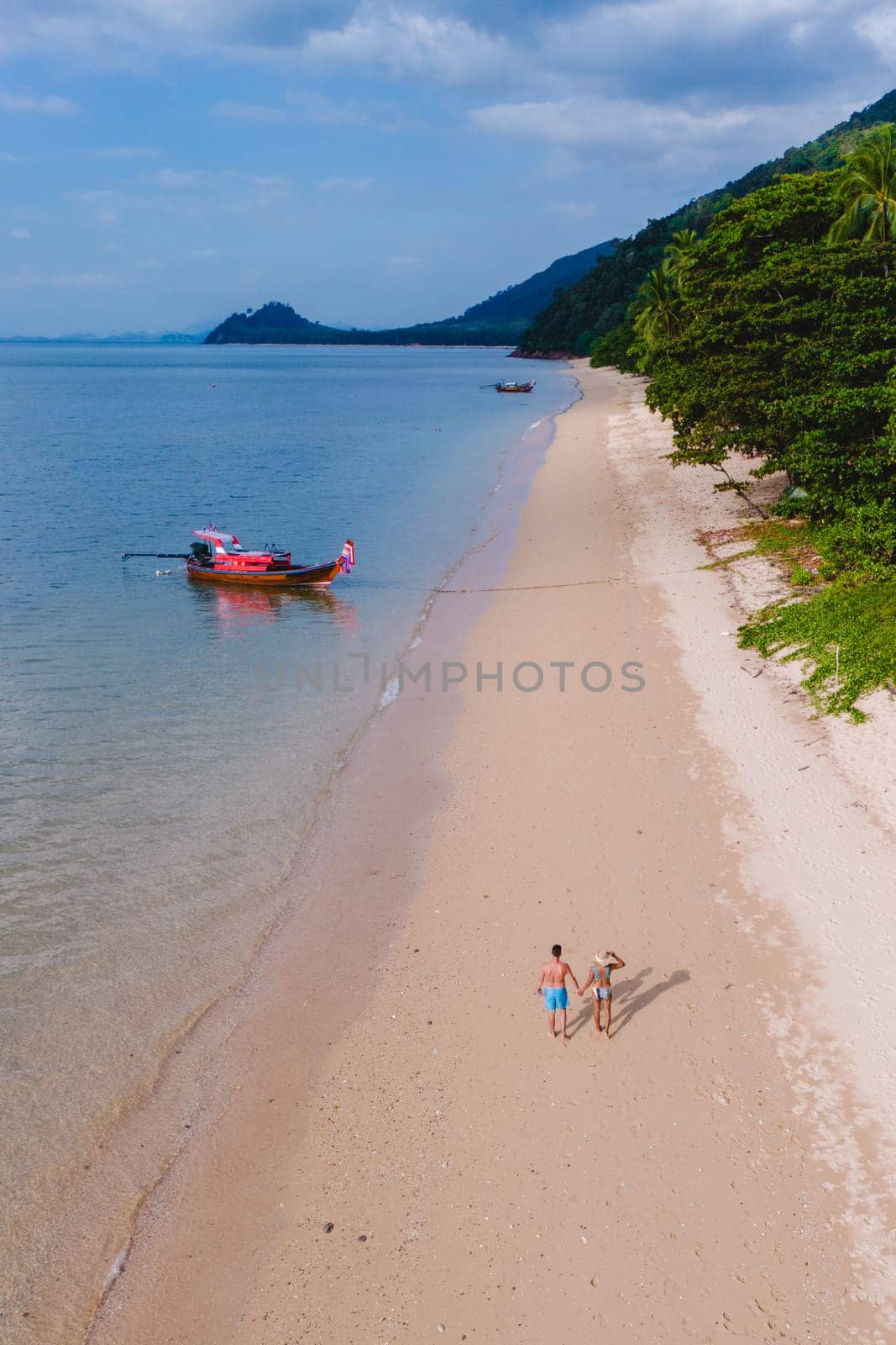 A beautiful view of a calm beach with crystal clear water on the blue sky at Koh Libong, Trang province, Thailand, Andaman Sea. A couple of men and woman walking on the beach on a sunny evening