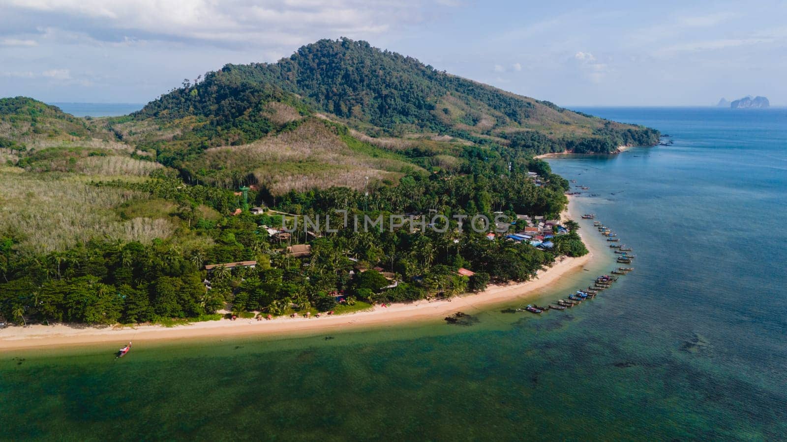 A beautiful view of a calm beach with crystal clear water on the blue sky at Koh Libong, Trang province, Thailand, Andaman Sea with mountains on the beackground