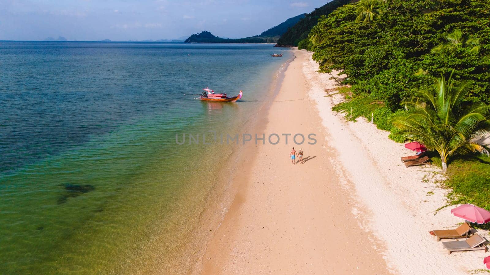 A beautiful view of a calm beach with crystal clear water on the blue sky at Koh Libong, Trang province, Thailand, Andaman Sea. A couple of men and woman walking on the beach on a sunny evening