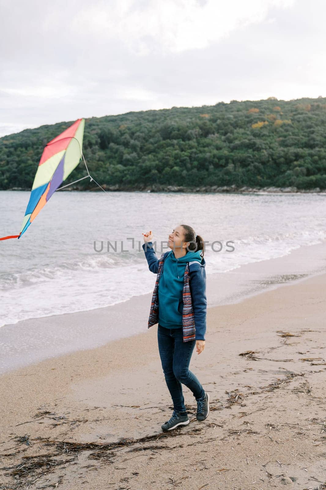 Smiling girl walking along the seashore with a colorful kite on a string. High quality photo
