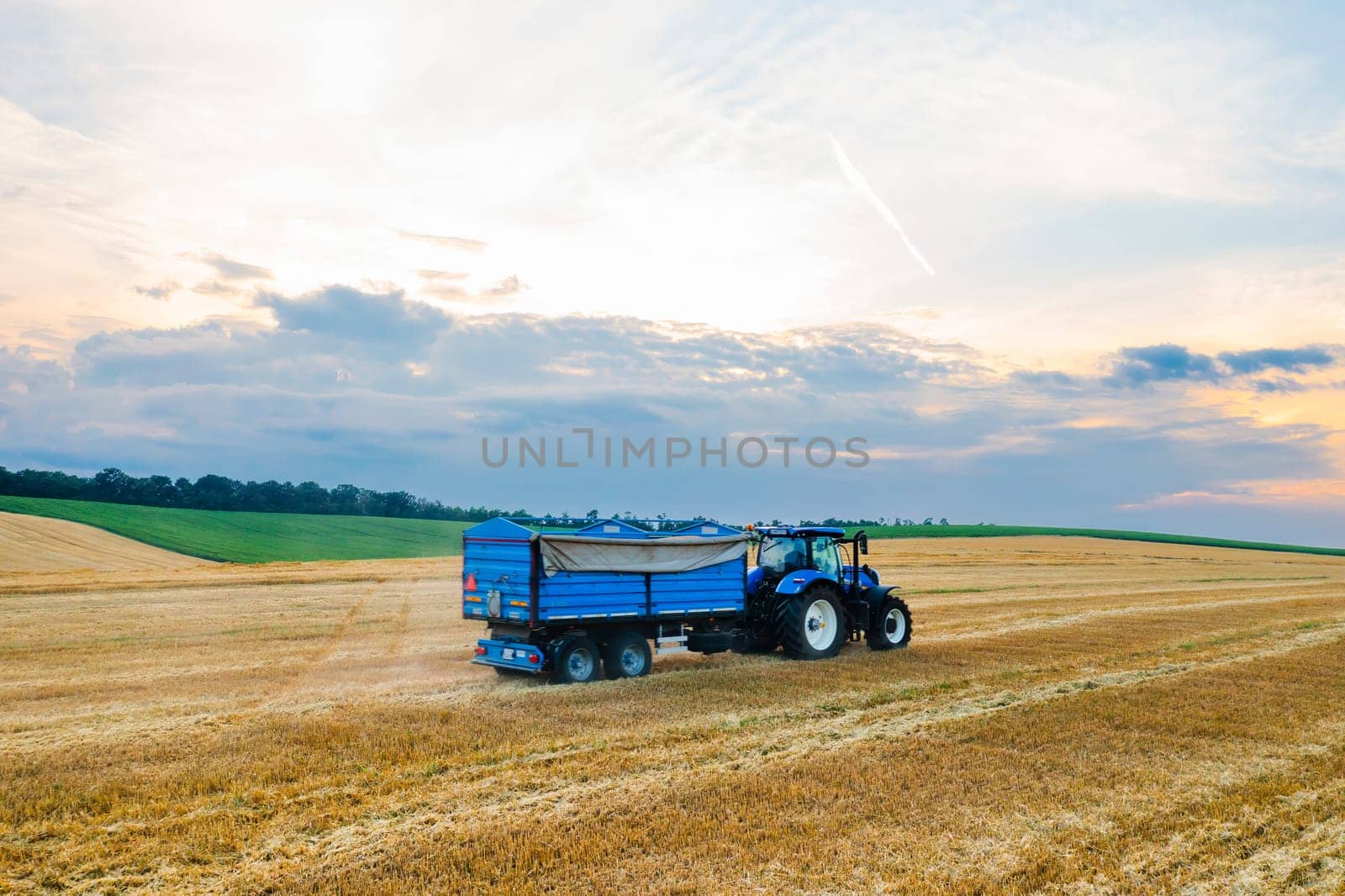 Tractor with trailer drives along reaped agricultural field by vladimka