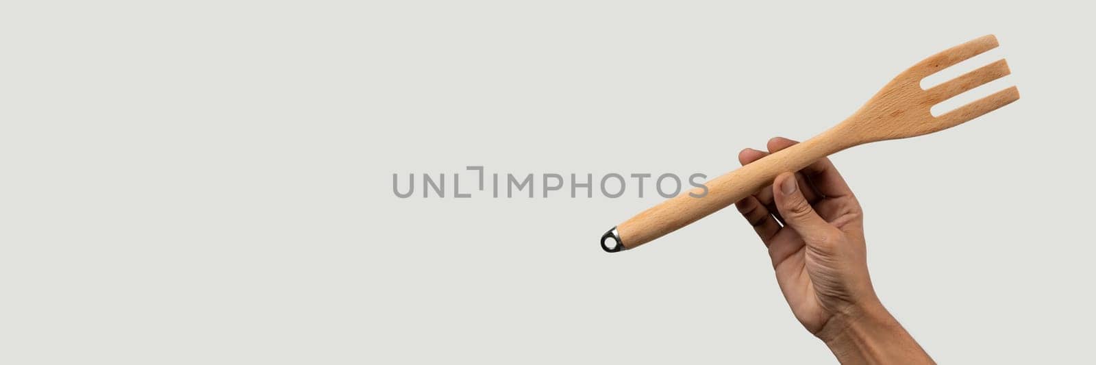 Hand holding wooden fork on grey background banner. High quality photo