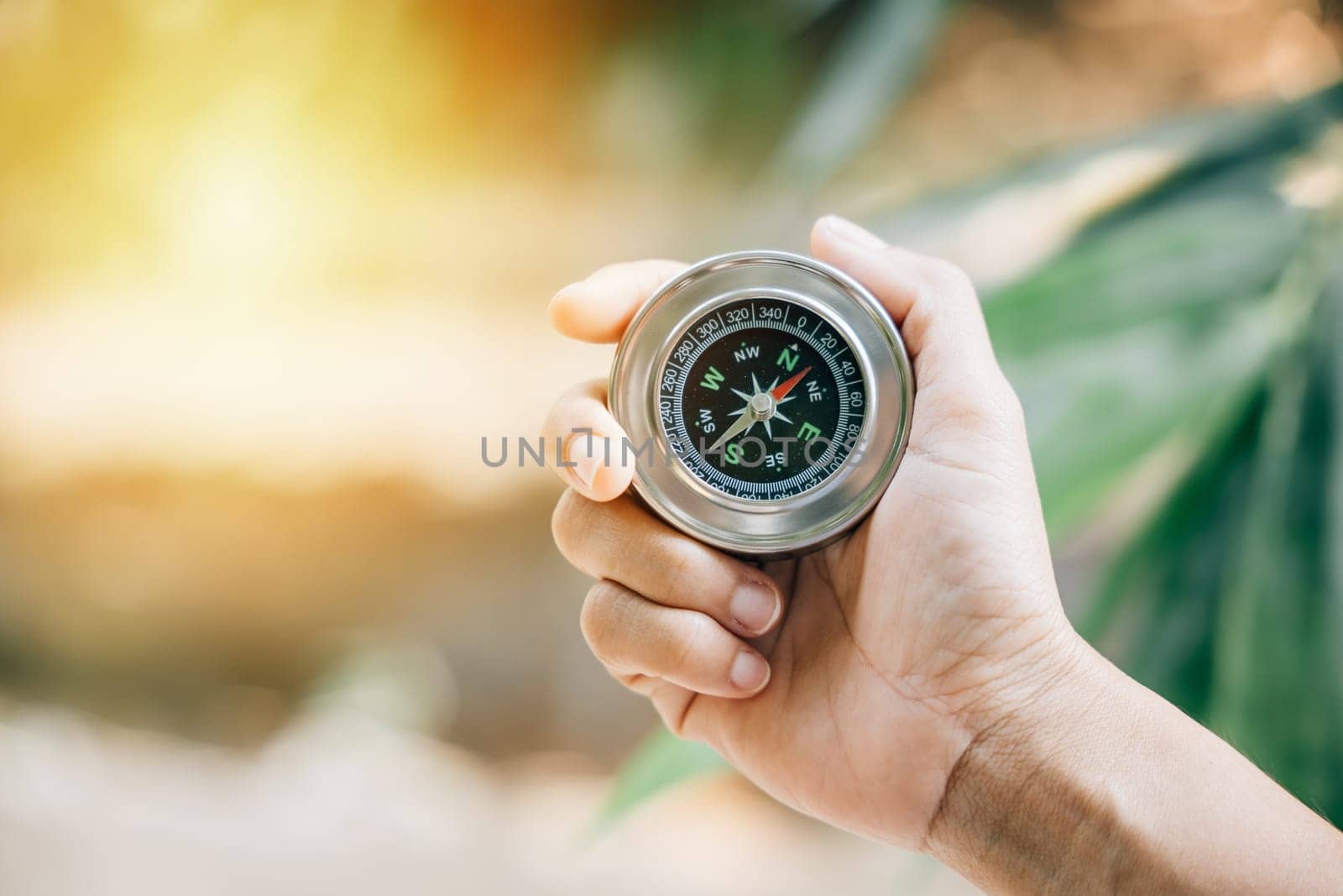 Hiker searches for direction in the forest holding a compass to overcome confusion. The compass in the hand signifies exploration and finding one way in the wilderness.