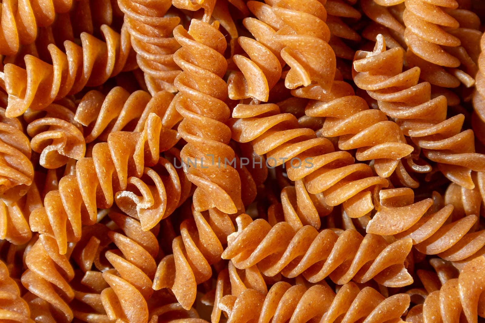 Uncooked Whole Grain Fusilli Pasta Background by InfinitumProdux