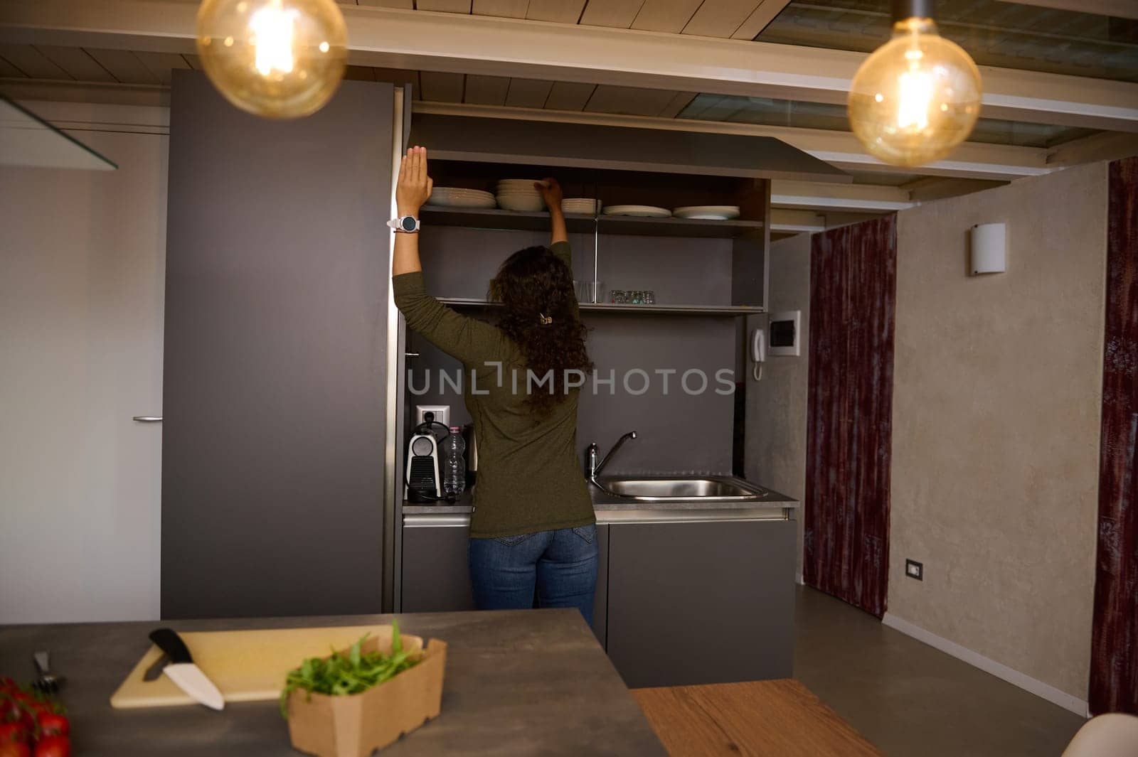 Rear view of brunette woman, a pretty housewife taking out plates from kitchen cabinet. People. Lifestyle. Domestic life by artgf