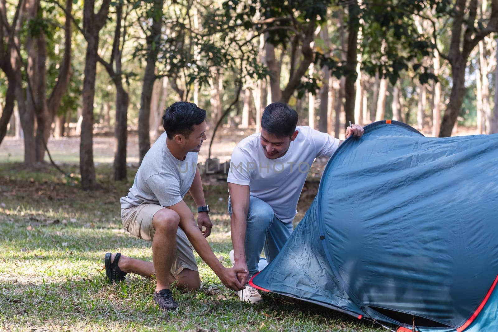 Asian LGBTQ couple camping together Set up a tent on the grass during the weekend by wichayada
