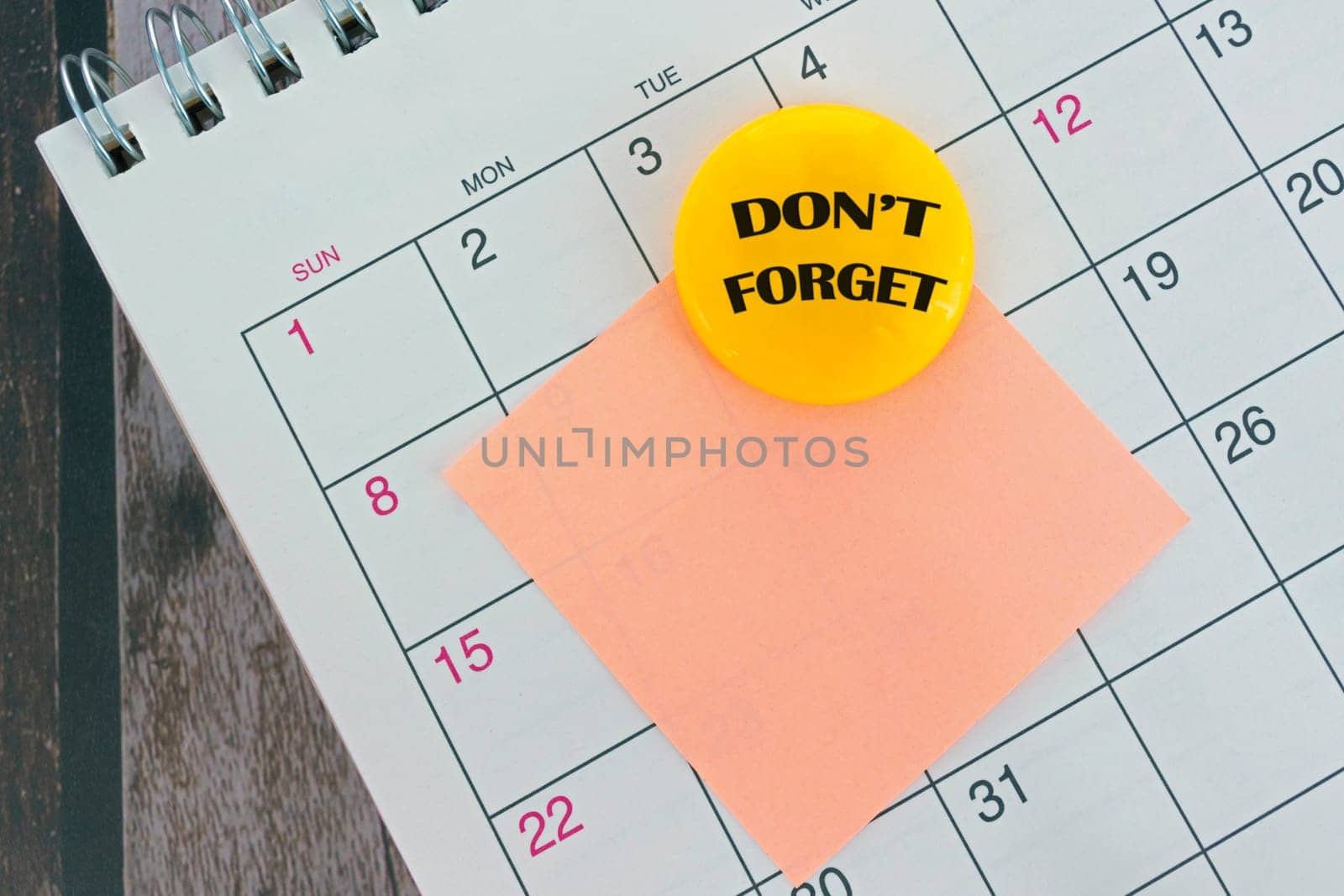 Orange paper sticky note with yellow magnet on calendar background. Copy space.