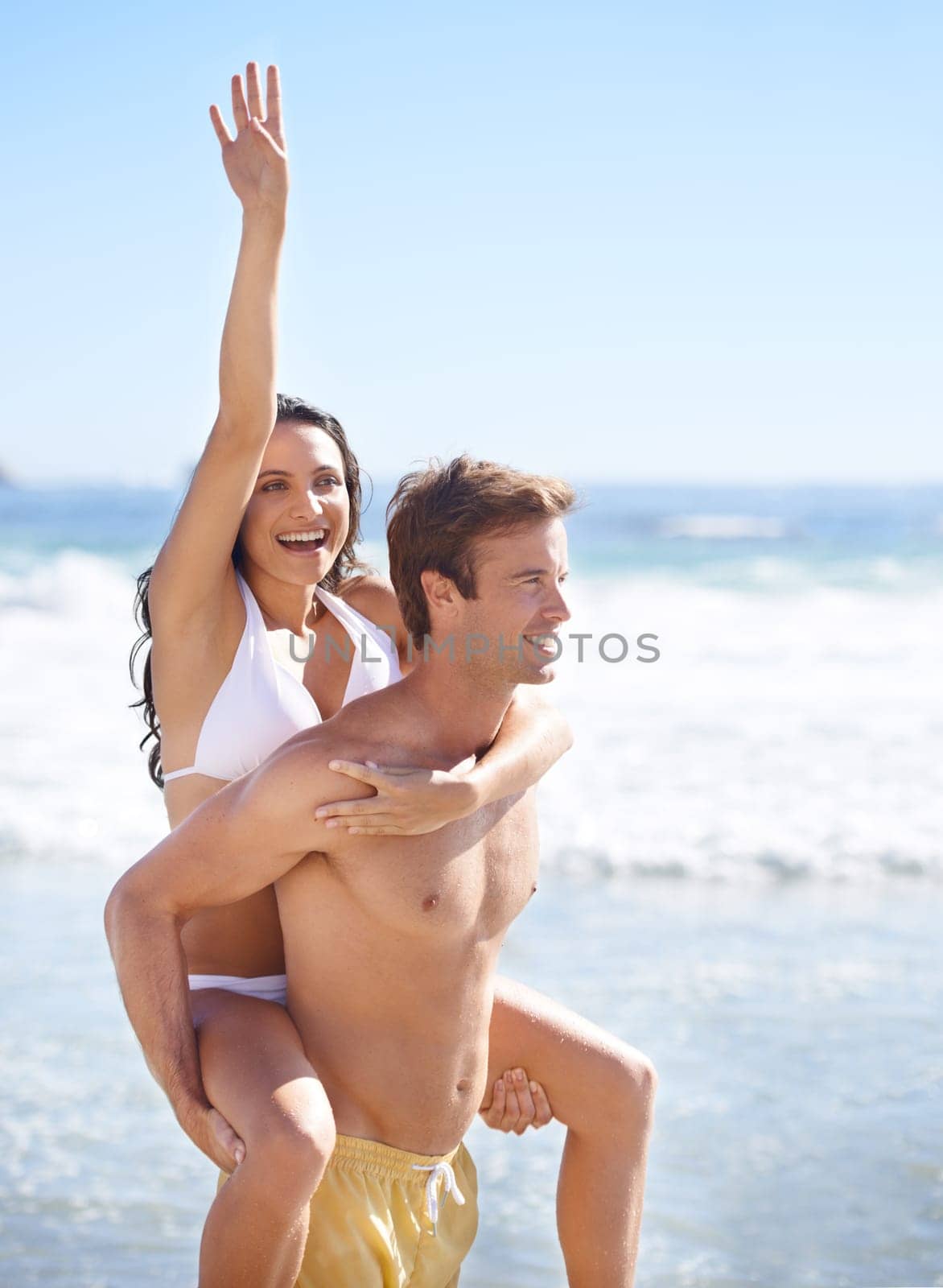 Piggy back, waves and happy couple on beach for holiday adventure together on tropical island on blue sky. Love, man and excited woman on ocean vacation with fun, romance and smile on travel in Bali