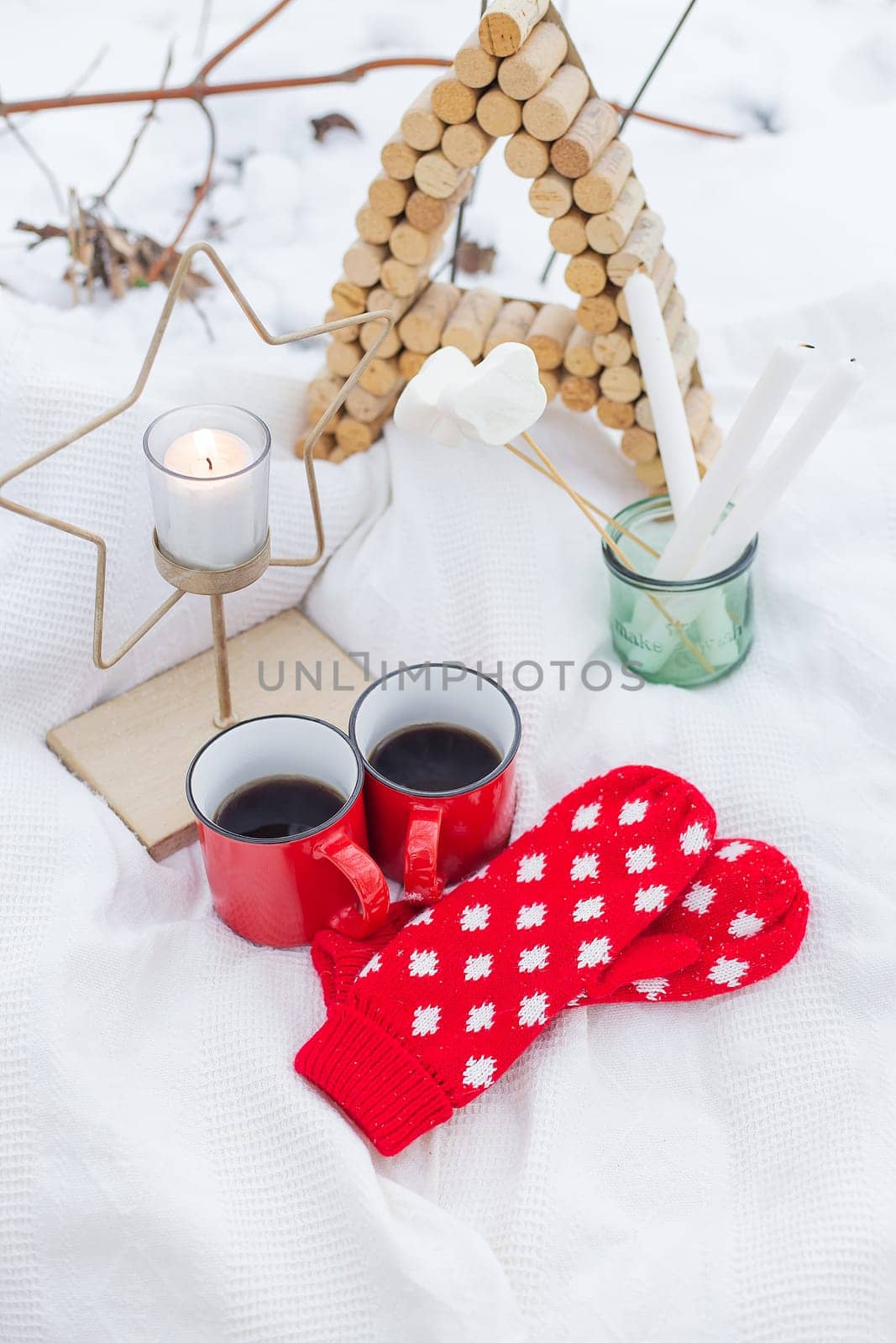 A cozy winter scene with hot drinks, mittens, and a candle on a snowy surface. Perfect for holiday cards and winter-themed designs