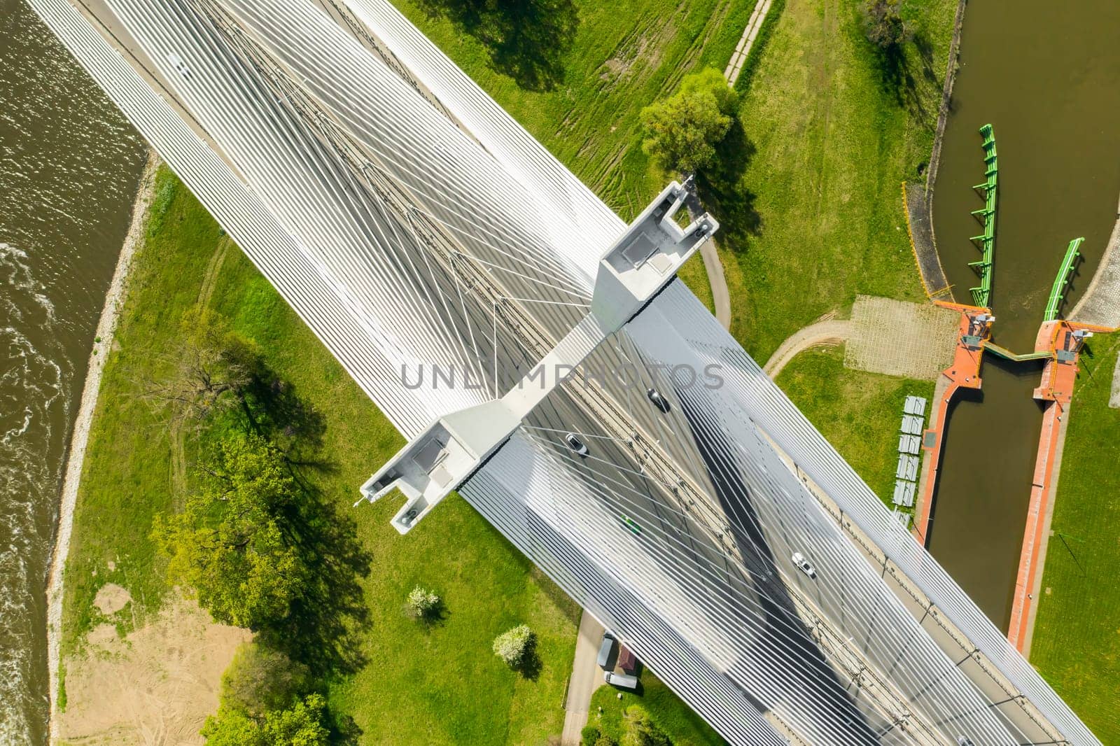 Top view of cable-stayed pylon bridge above urban parks with green grass.