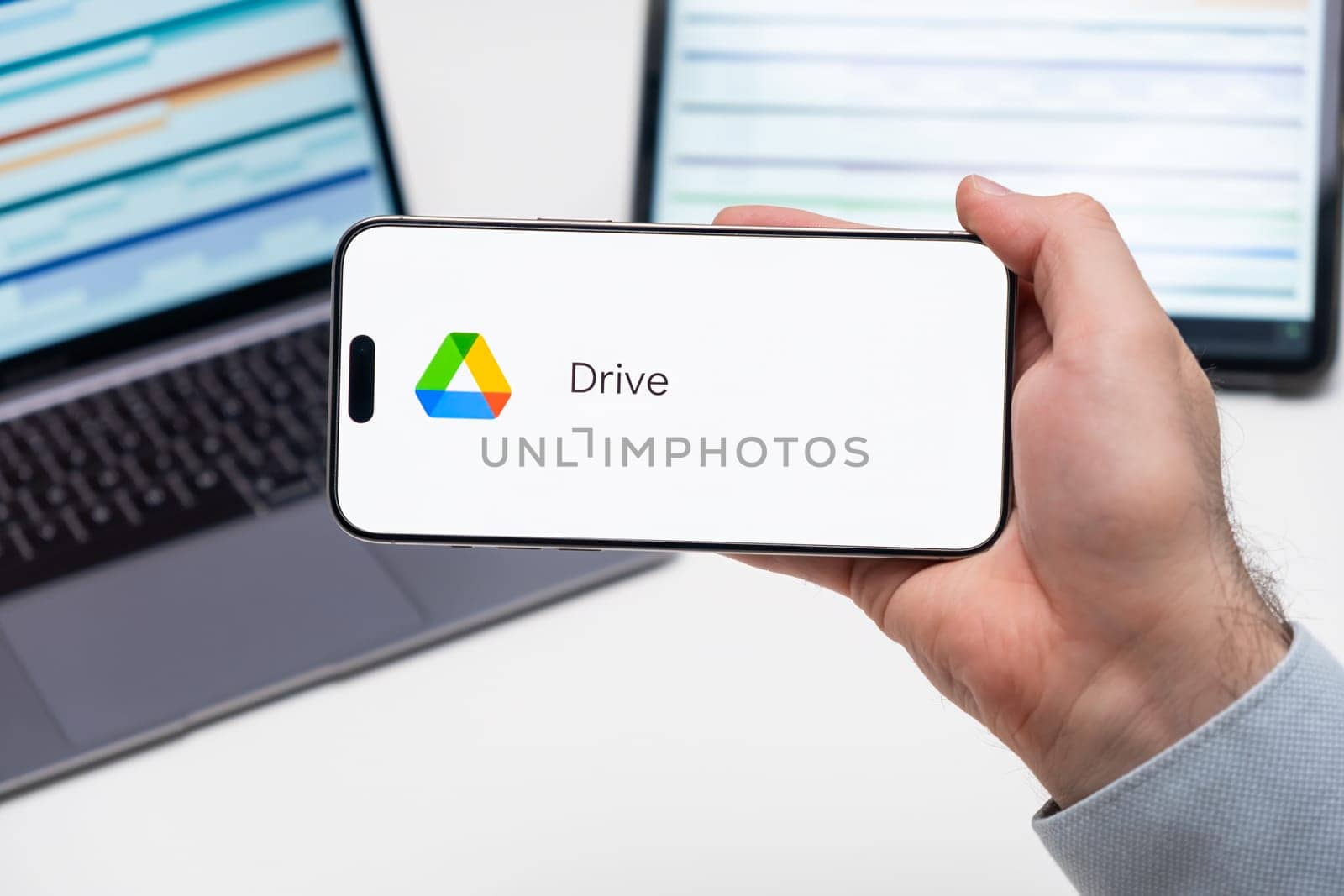 Google Drive application logo on the screen of smart phone in mans hand, laptop and tablet are on the table in the background, December 2023, Prague, Czech Republic.