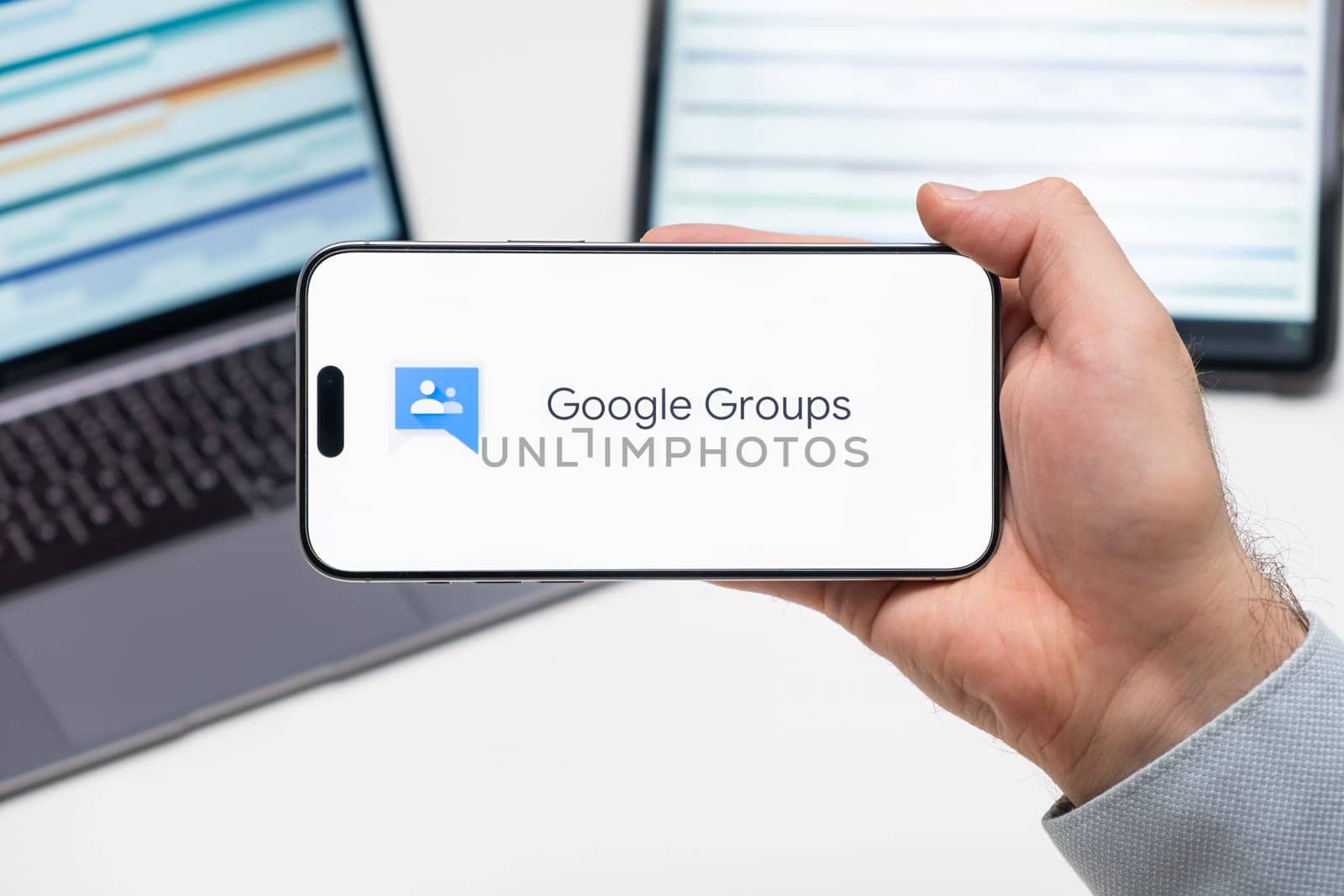 Google Groups logo of app on the screen of mobile phone held by man in front of the laptop and tablet by vladimka