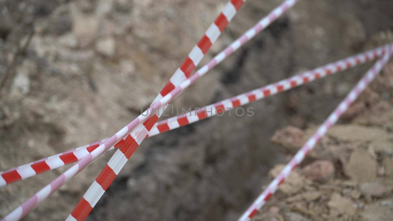 Red white barrier tape trenches. Focus on red and white barrier tape at construction site. Ribbons indicate dug trenches. by Matiunina