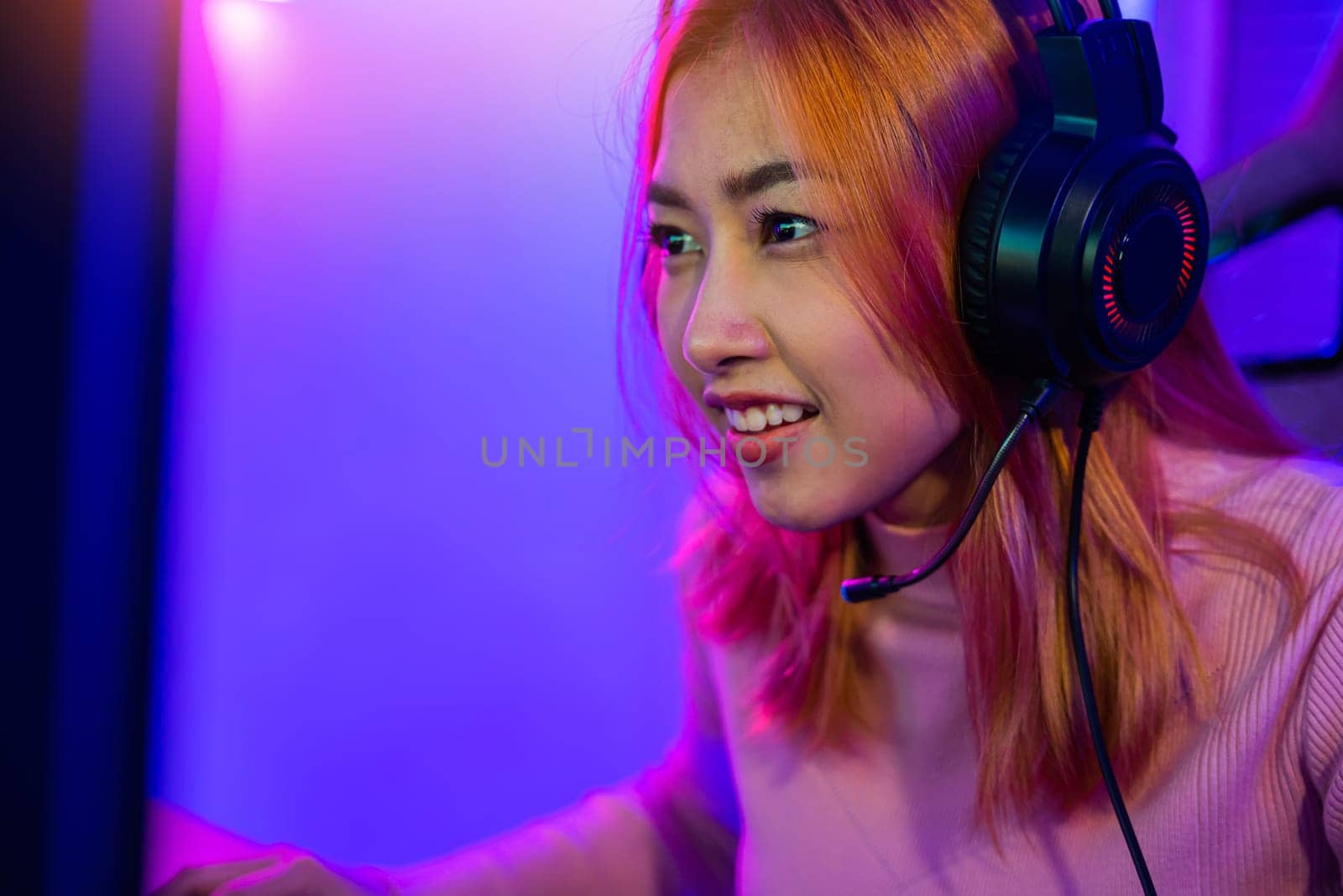 Happy Gamer endeavor plays online video games tournament with computer neon lights, young woman wearing gaming headphones intend to do playing live stream games online at home