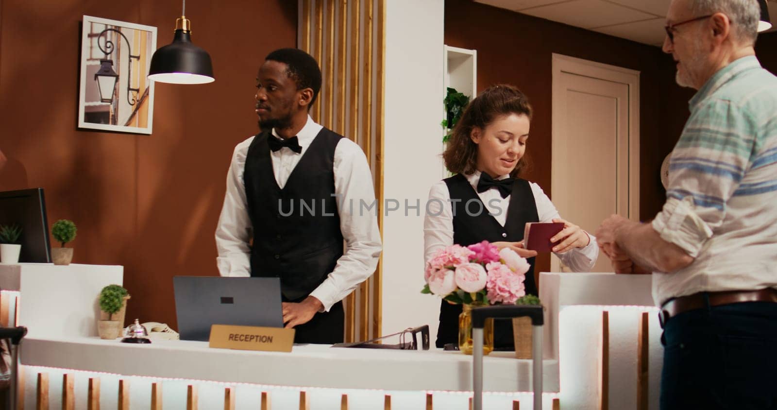 Front desk staff checking passports for tourists with room reservation at five star hotel, looking at id documents in reception lobby. Diverse employees assisting senior couple.