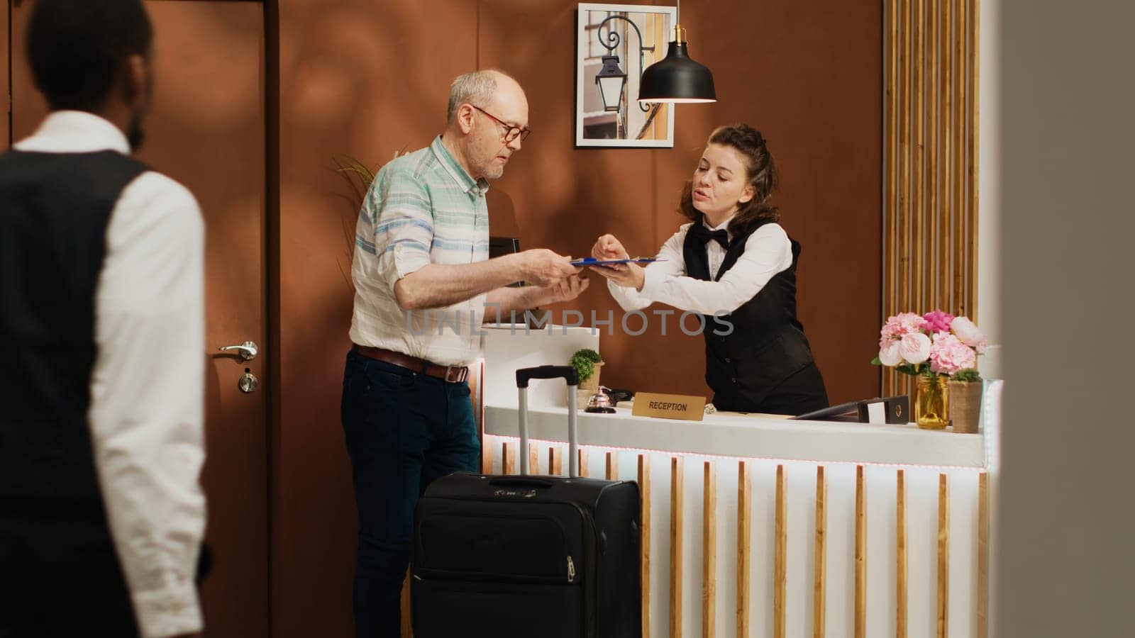 Senior guy at front desk doing check in routine in expensive five star hotel lobby. Traveller signing registration forms at front desk, checking room service and ammenities on holiday trip.
