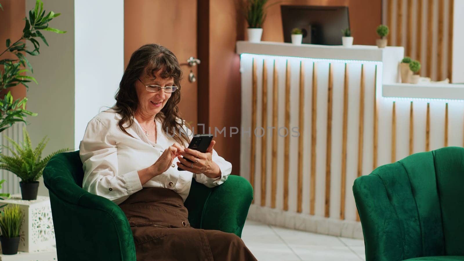 Old person checking text messages after long flight, waiting for check in process at five star hotel. Senior woman browsing smartphone apps in lounge area, relaxing in lobby.