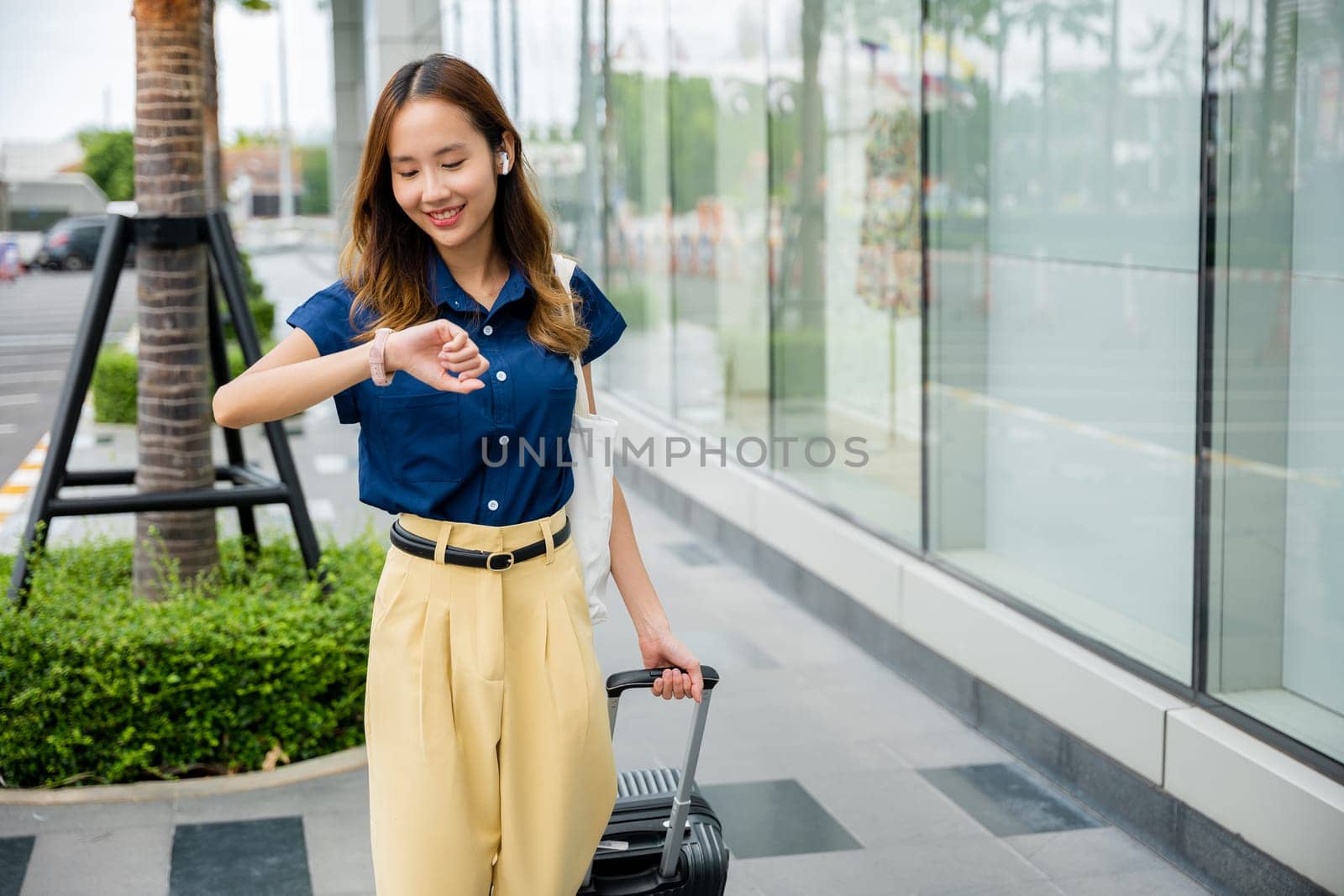 Young woman traveler waiting for her flight at the airport with her luggage and looking at the flight information display board. Time management and punctuality concept.