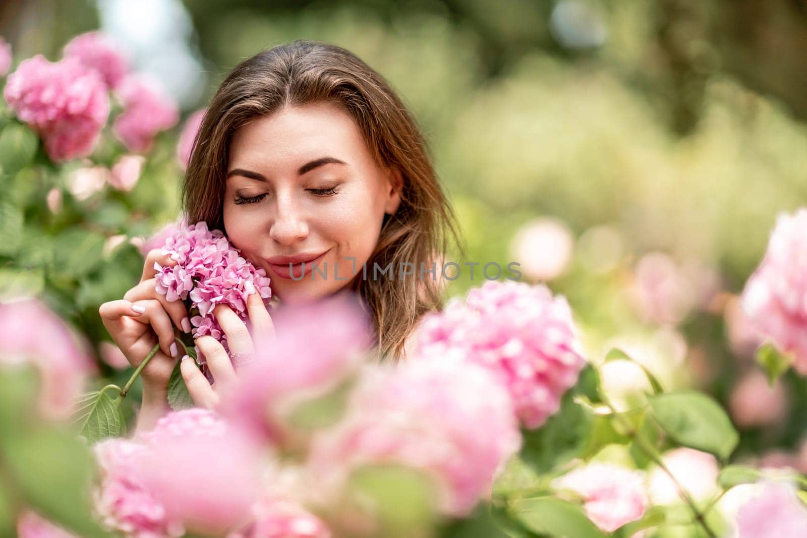 Hydrangeas Happy woman in pink dress amid hydrangeas. Large pink hydrangea caps surround woman. Sunny outdoor setting. Showcasing happy woman amid hydrangea bloom. by Matiunina