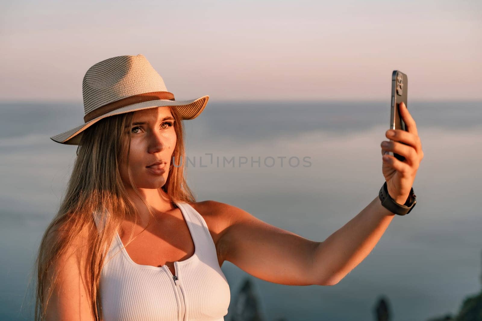 Selfie woman in hat, white tank top and shorts makes selfie shot mobile phone post photo social network outdoors on sea background beach people vacation lifestyle travel concept