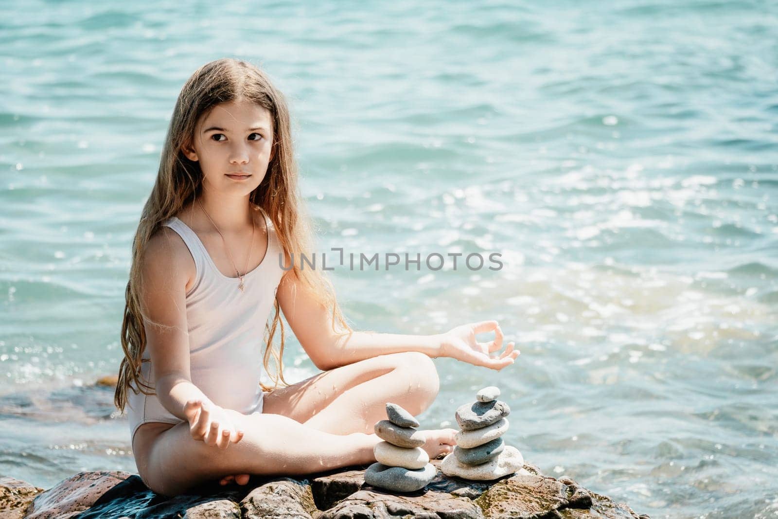 Woman with daughter bilds stones pyramid on seashore on a sunny day on the blue sea background. Happy family holidays. Pebble beach, calm sea. Concept of happy vacation on the sea, meditation, spa by panophotograph