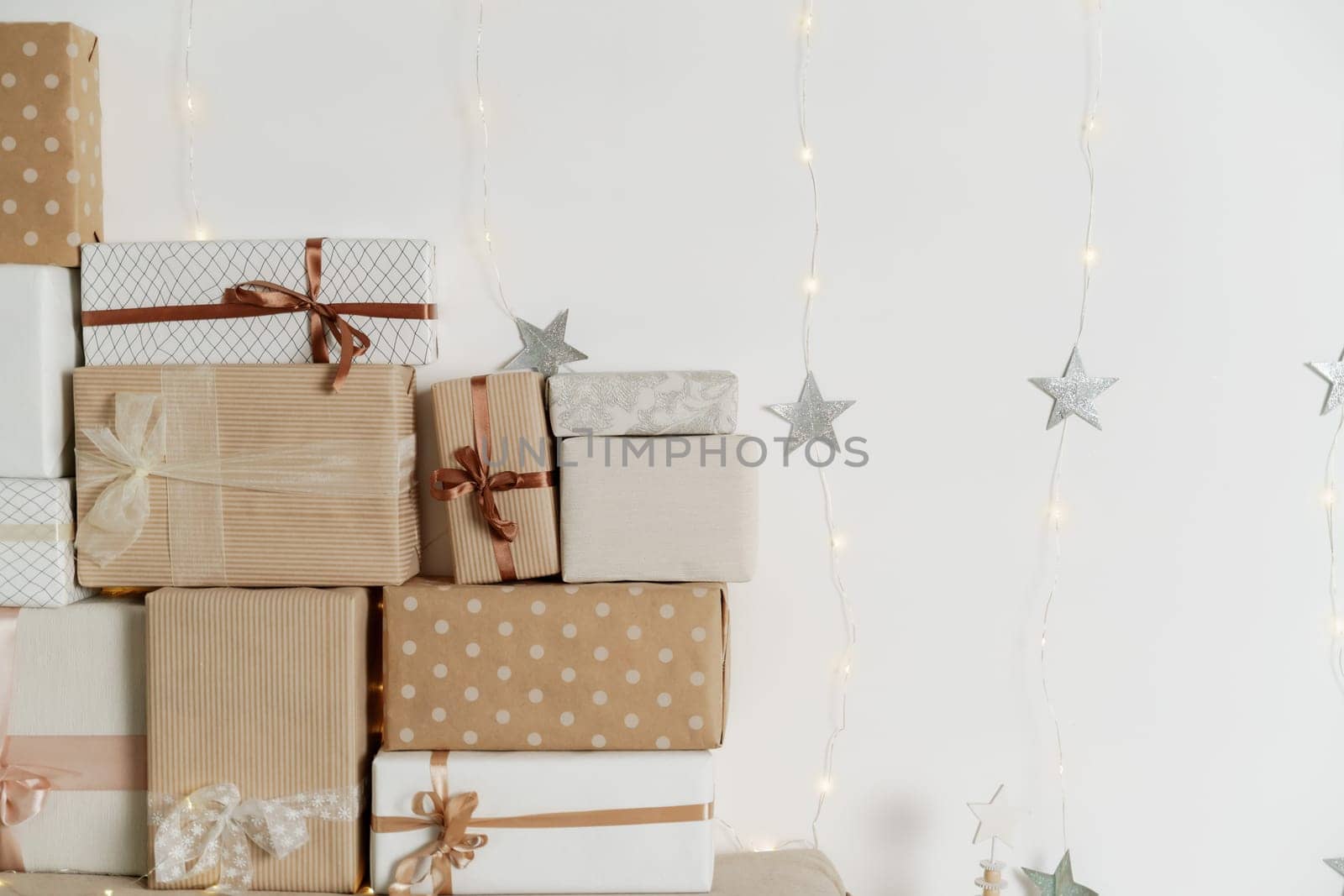 Pile of Christmas gifts in colorful wrapping with ribbons against a white wall with silver stars. by Matiunina
