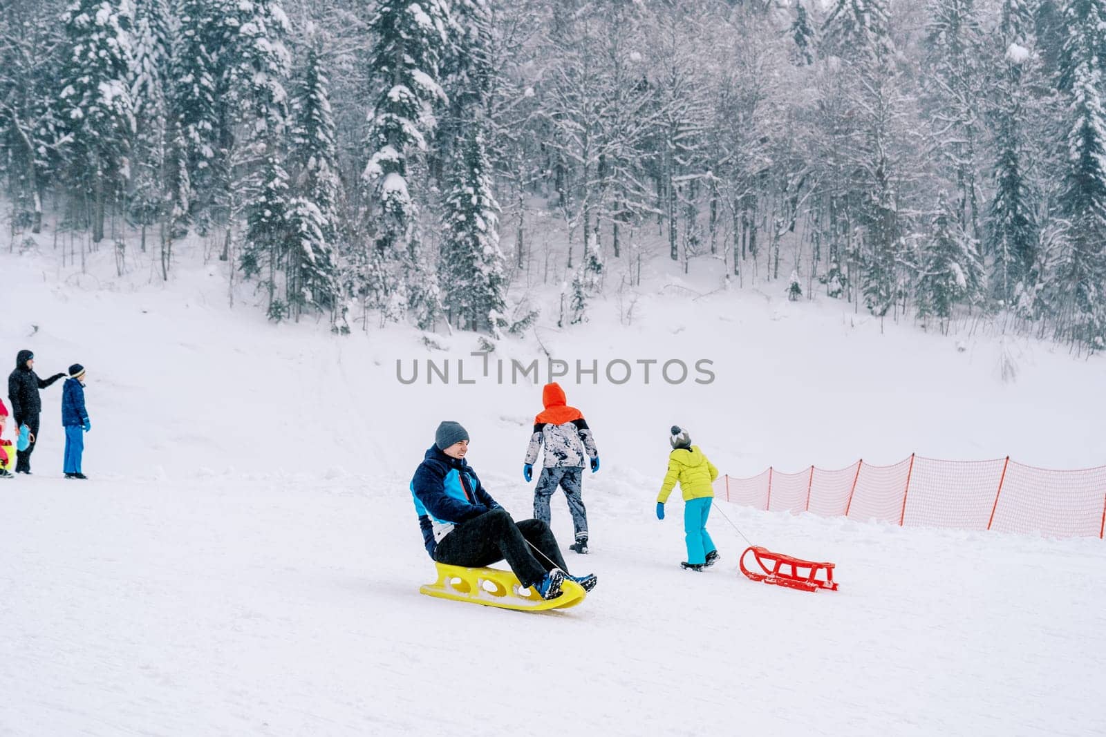 Young man rides a sled on a snow-covered mountain past climbing sledders. High quality photo