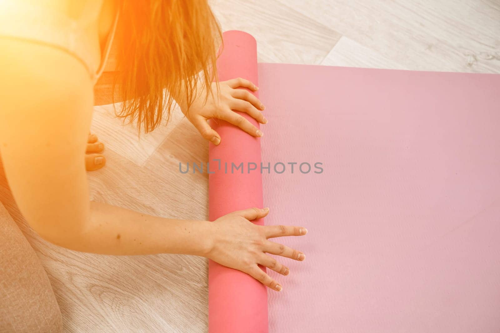 A young woman rolls a pink fitness or yoga mat before or after exercising, exercising at home in the living room or in a yoga studio. Healthy habits, keep fit, weight loss concept. Closeup photo.