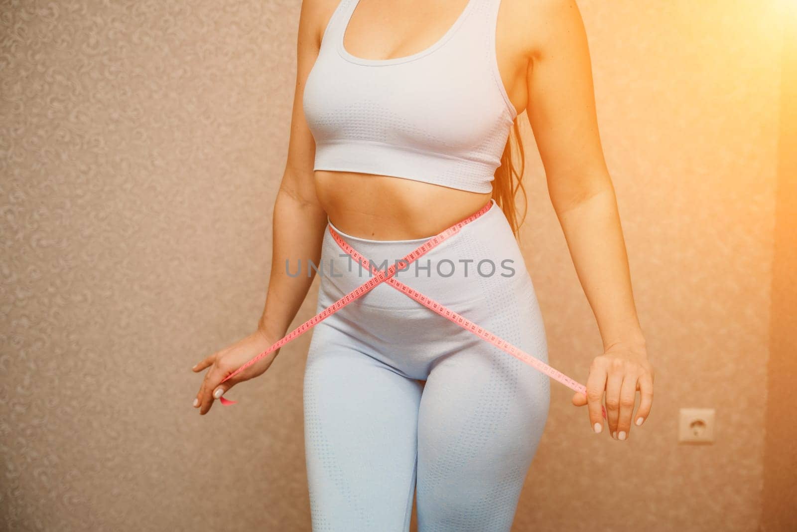 Cropped view of slim woman measuring waist with tape measure at home, close up. Unrecognizable european woman checking the result of diet for weight loss or liposuction indoors by Matiunina