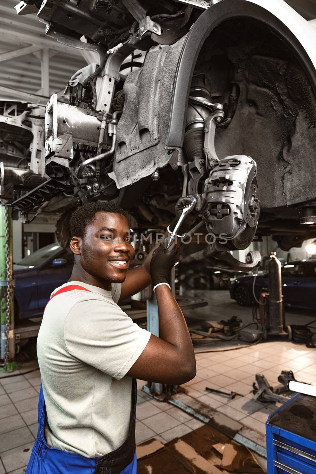 African male auto-mechanic repairing car brakes under the car in auto service by Fabrikasimf