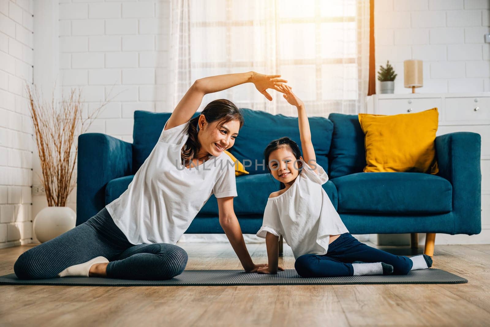 A mother and her little daughter practice yoga together focusing on relaxation and balance in the cozy living room by Sorapop