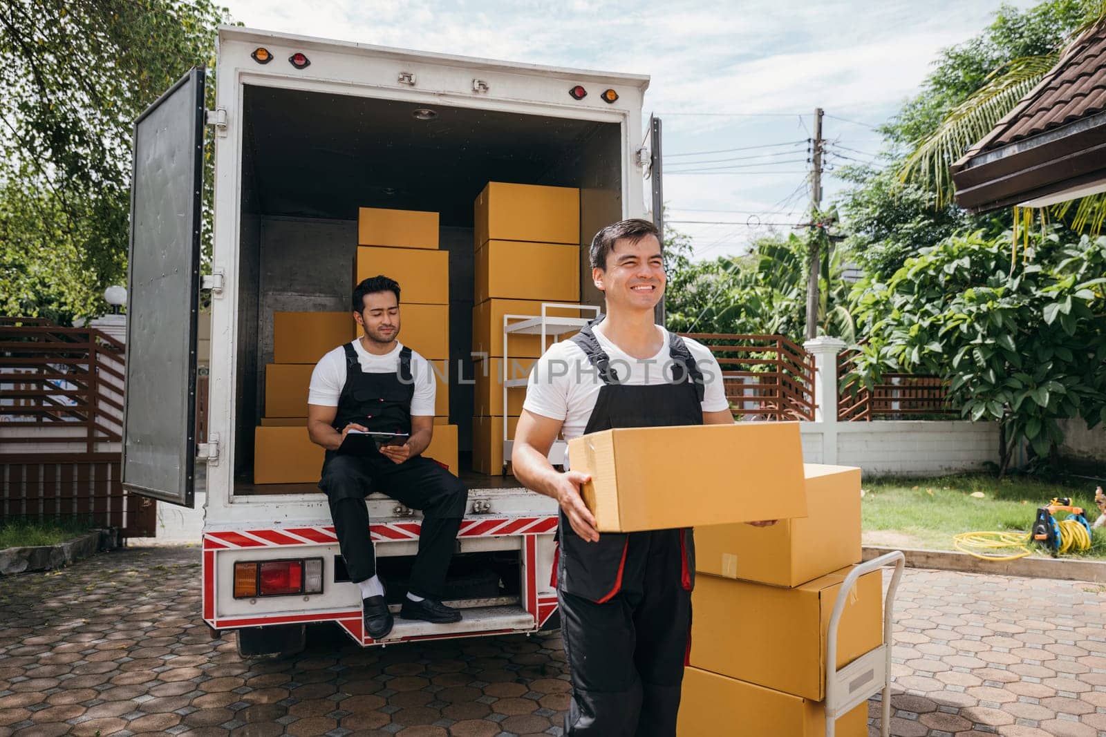 Movers unload boxes from a truck outdoors. Delivery service workers cooperate in relocation service. Teamwork among colleagues. Smiling employees carrying boxes. relocation cooperation Moving Day by Sorapop