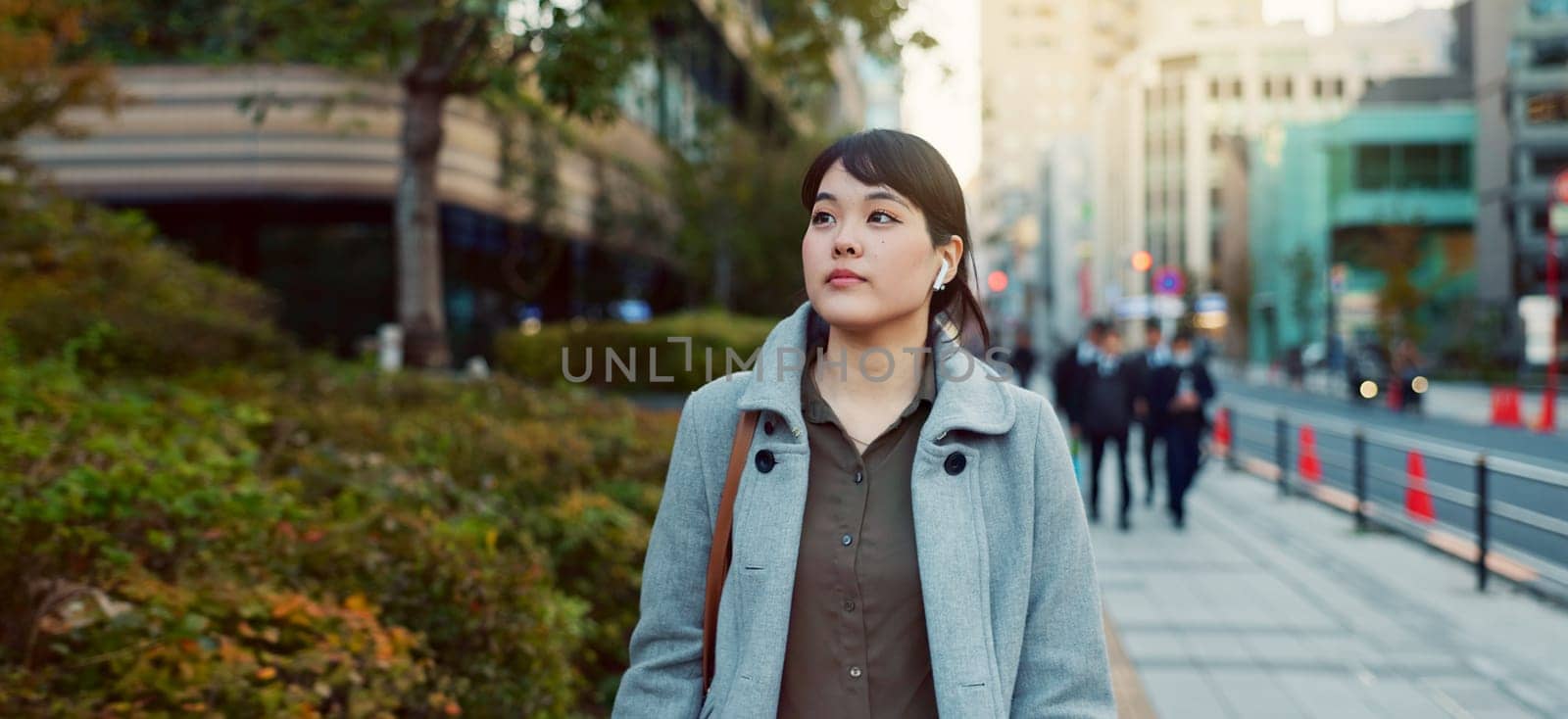 Woman, Asian and walking, travel or commute to work with professional in city with earphones. Listening to music on journey, podcast and commuter on urban street or sidewalk in Tokyo with playlist by YuriArcurs
