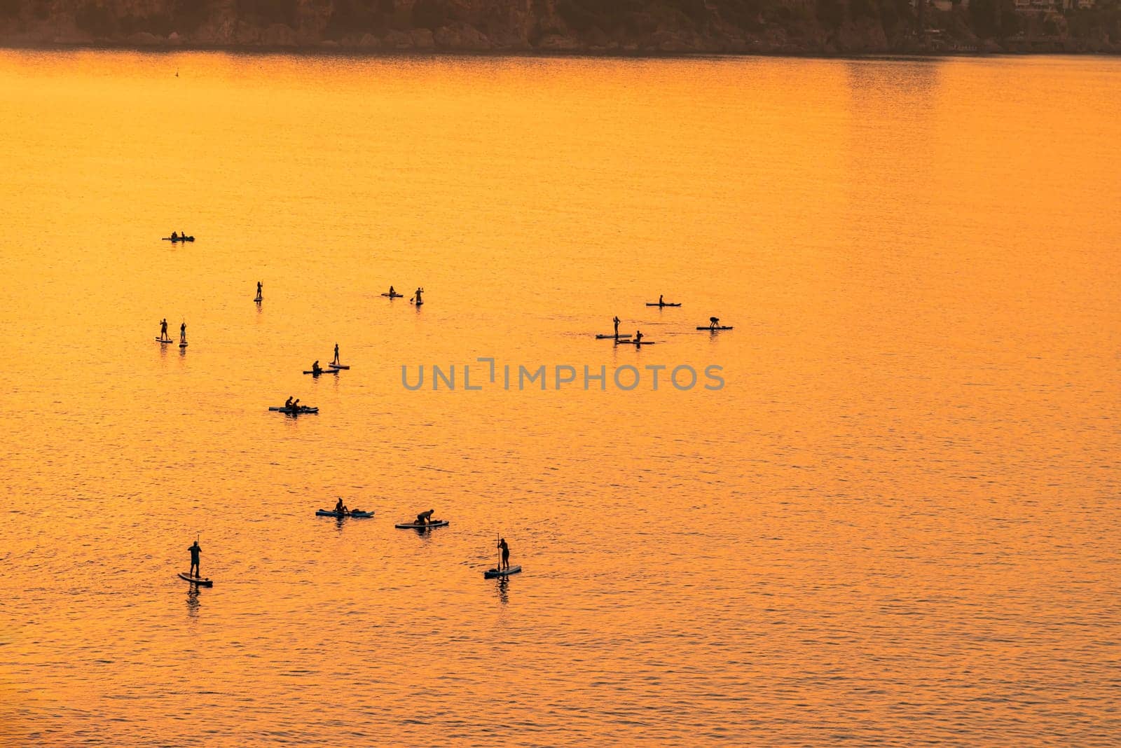 Adventurous people on a stand up paddle board is paddling during a bright and vibrant sunrise