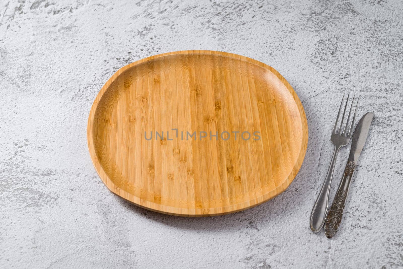 Wooden plate, fork and knife on white stone background. handmade kitchen utensils