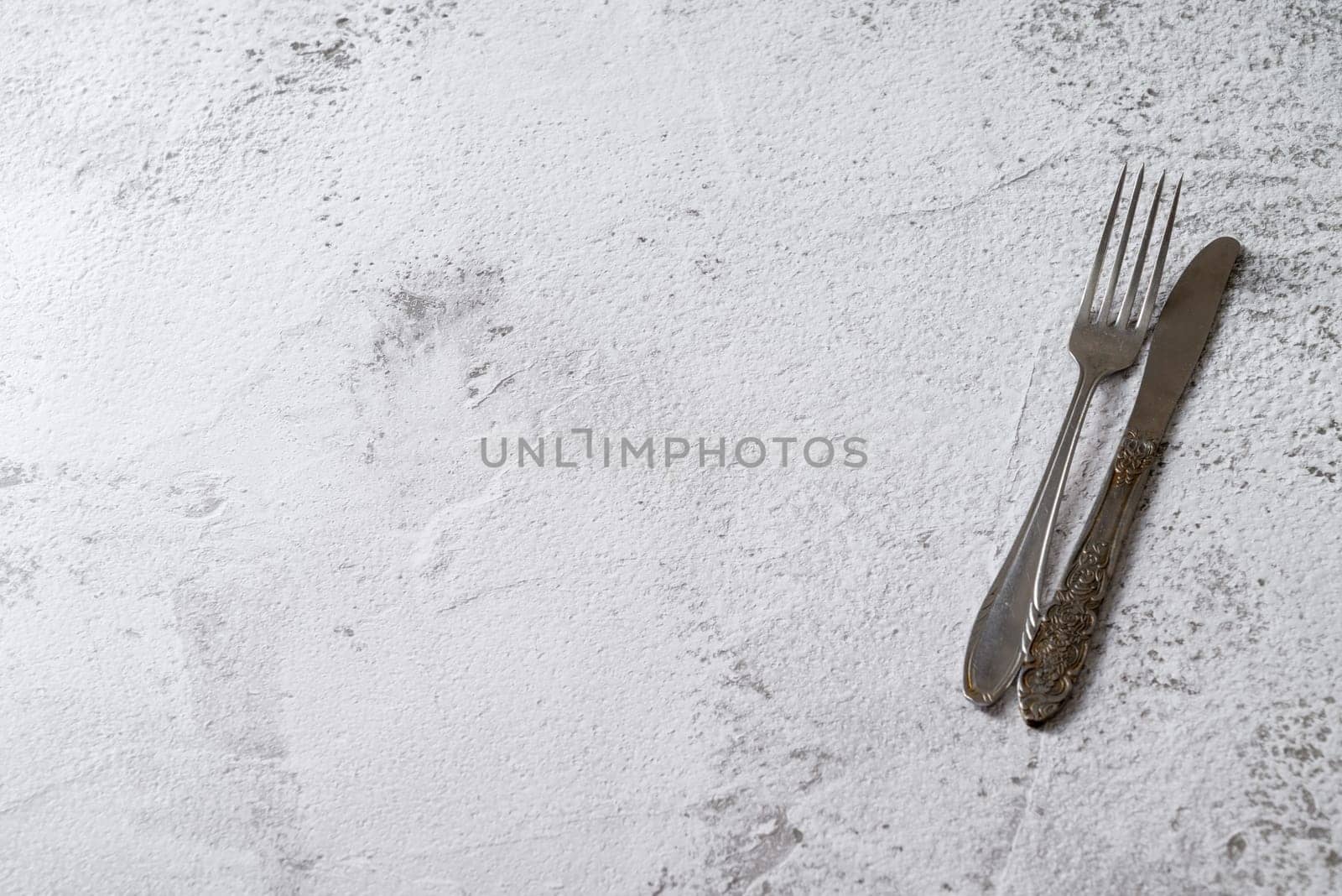 Antique fork and knife on white stone table by Sonat