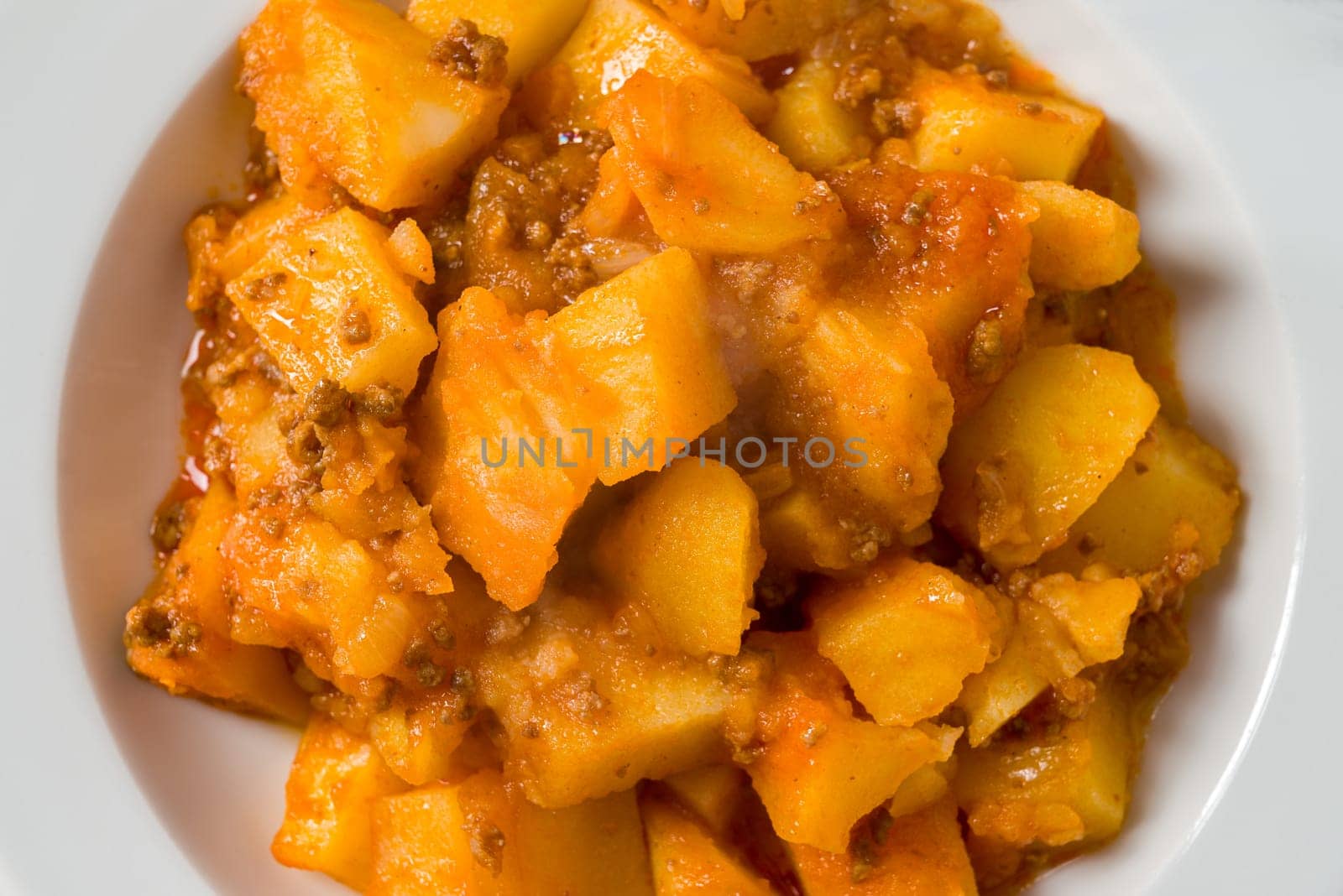 Minced meat and potato dish on white porcelain plate on stone table by Sonat