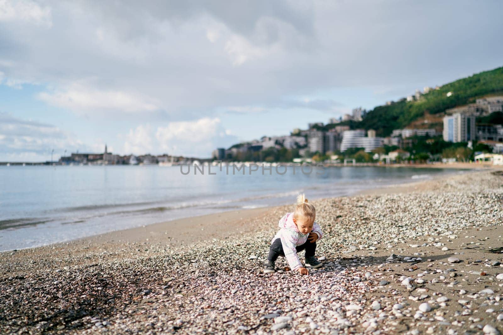 Little girl playing with pebbles on the beach squatting by Nadtochiy