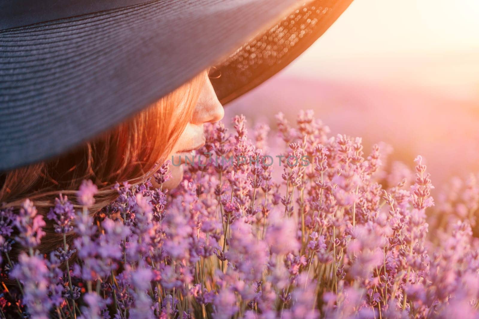 Woman lavender field. Happy carefree woman in black dress and hat with large brim smelling a blooming lavender on sunset. Perfect for inspirational and warm concepts in travel and wanderlust. Close up by panophotograph