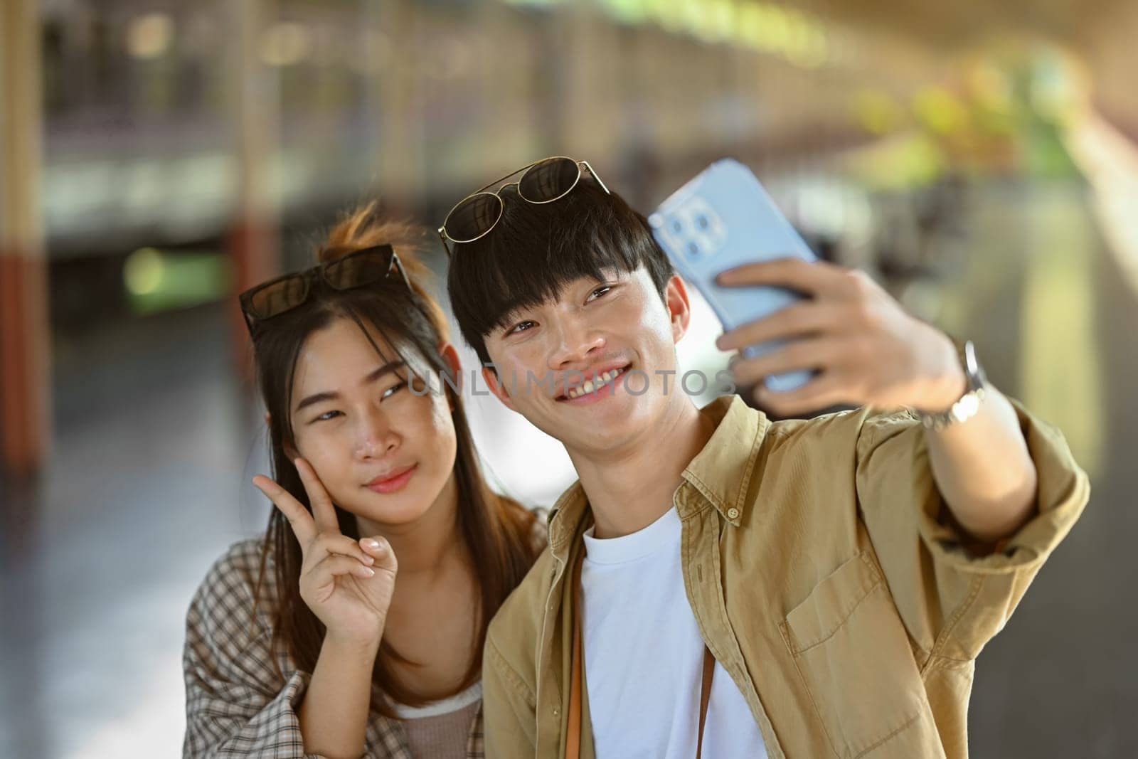 Attractive young couple taking a selfie with mobile phone at train station. Travel and lifestyle concept by prathanchorruangsak